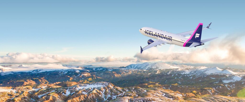 An Icelandair plane is flying above a rugged snow capped mountain range.