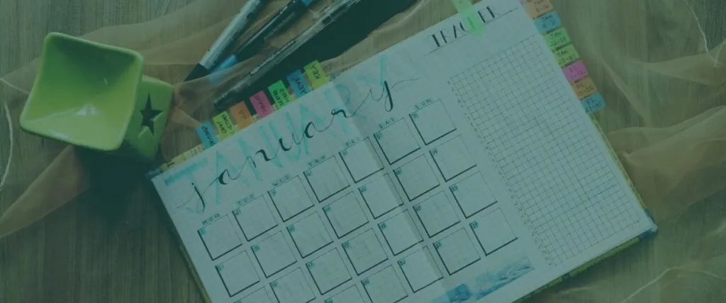 A monthly planner is open next to a pen pot indicating intention to plan ahead.