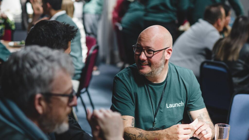 A Launch staff member is talking and smiling with someone in a busy room